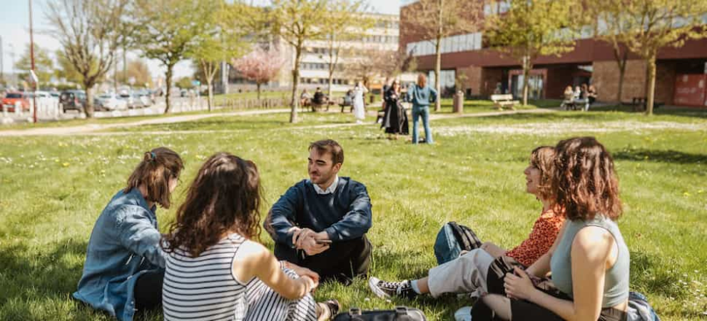 Des étudiants discutent, assis dans l'herbe, devant l'université du Mans.